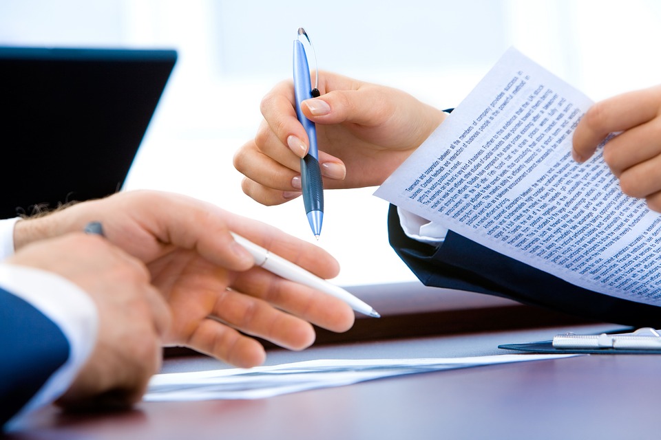 the hands of two men hold pens and paper across a desk